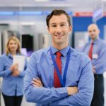 Portrait of salesman in retail store. Other members of the sales team can be seen standing in the background. Horizontal shot.